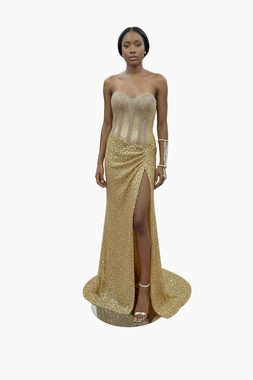 Woman wearing a gold strapless gown with a slit on a white background